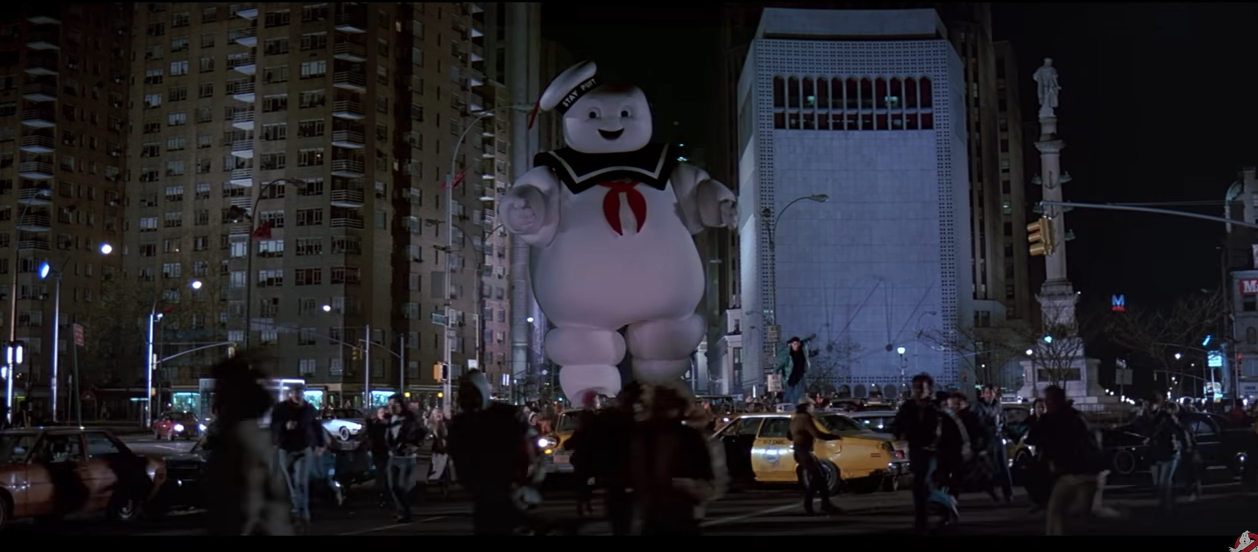 The Stay Puft Marshmallow Man from film Ghostbusters walks down a New York street as people flee in terror.